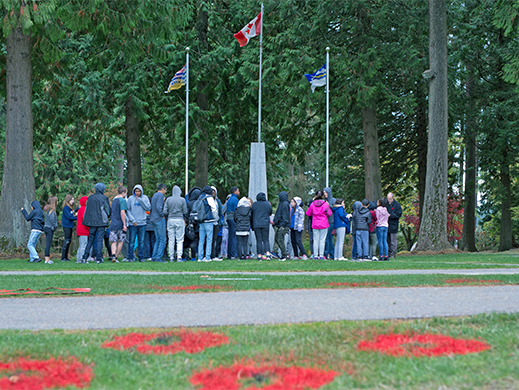 A group od people attending a Rememrance Day event with painted poppies on the grass
