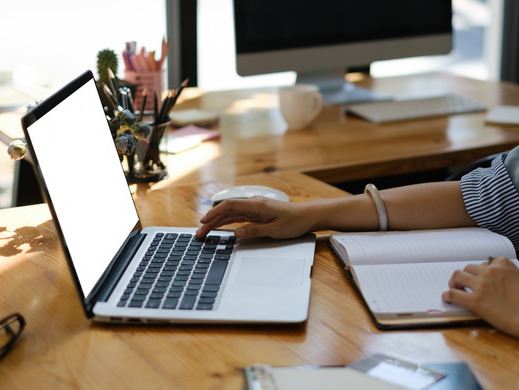 Image of laptop on a desk with a person's hand typing visible