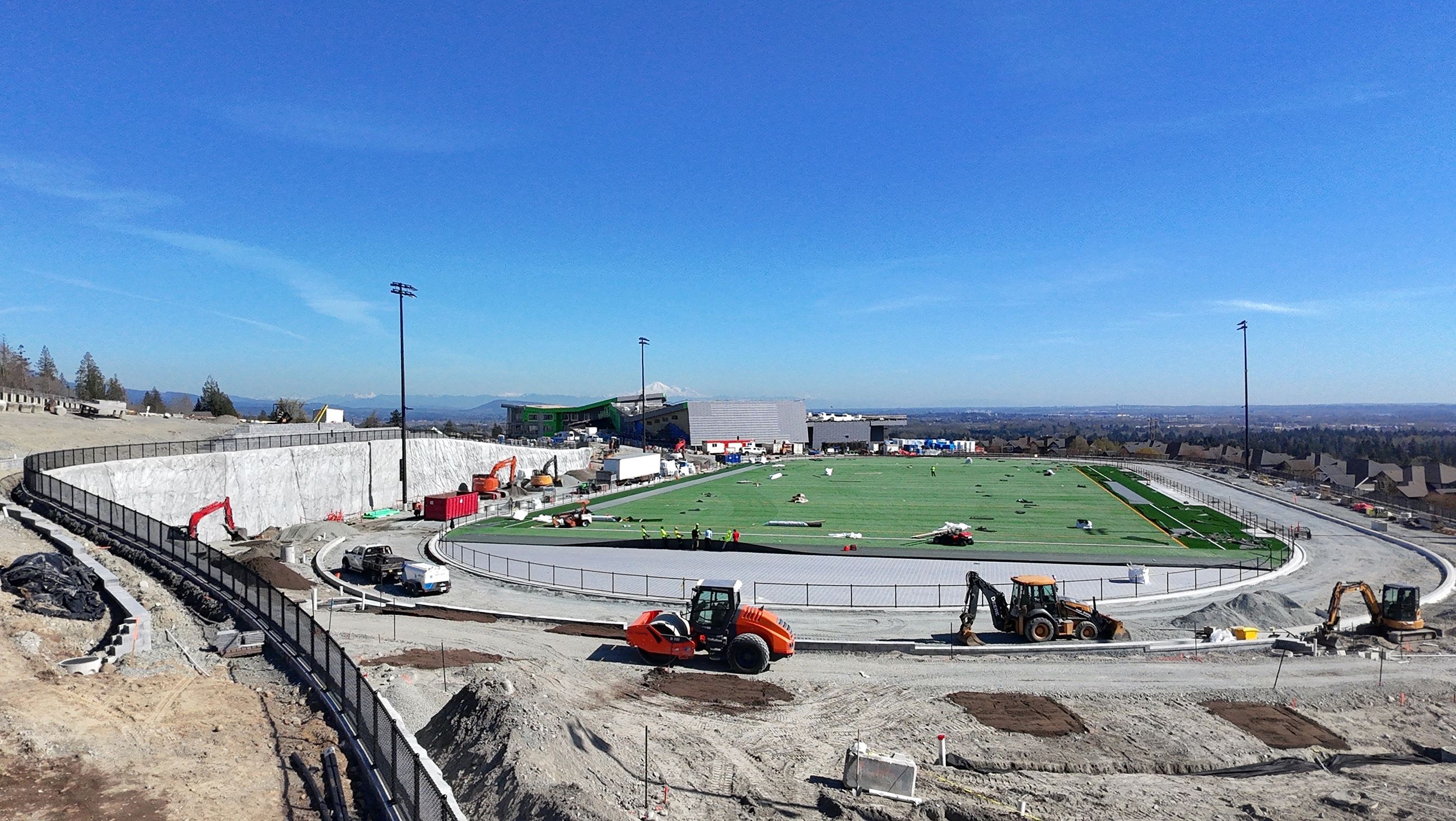 Looking south over the construction site, the bright green artificial turf field is being installed