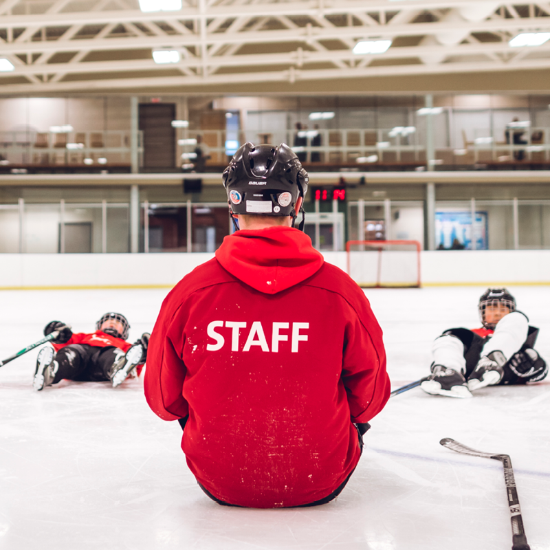 Hockey instructor with students sitting on the ice.