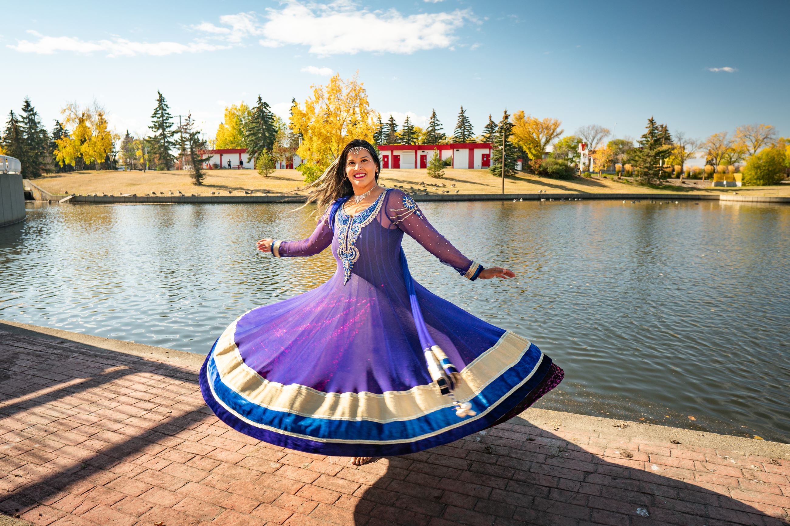 Karima Essa in a flared purple dress standing on a brick path on the edge of a small lake